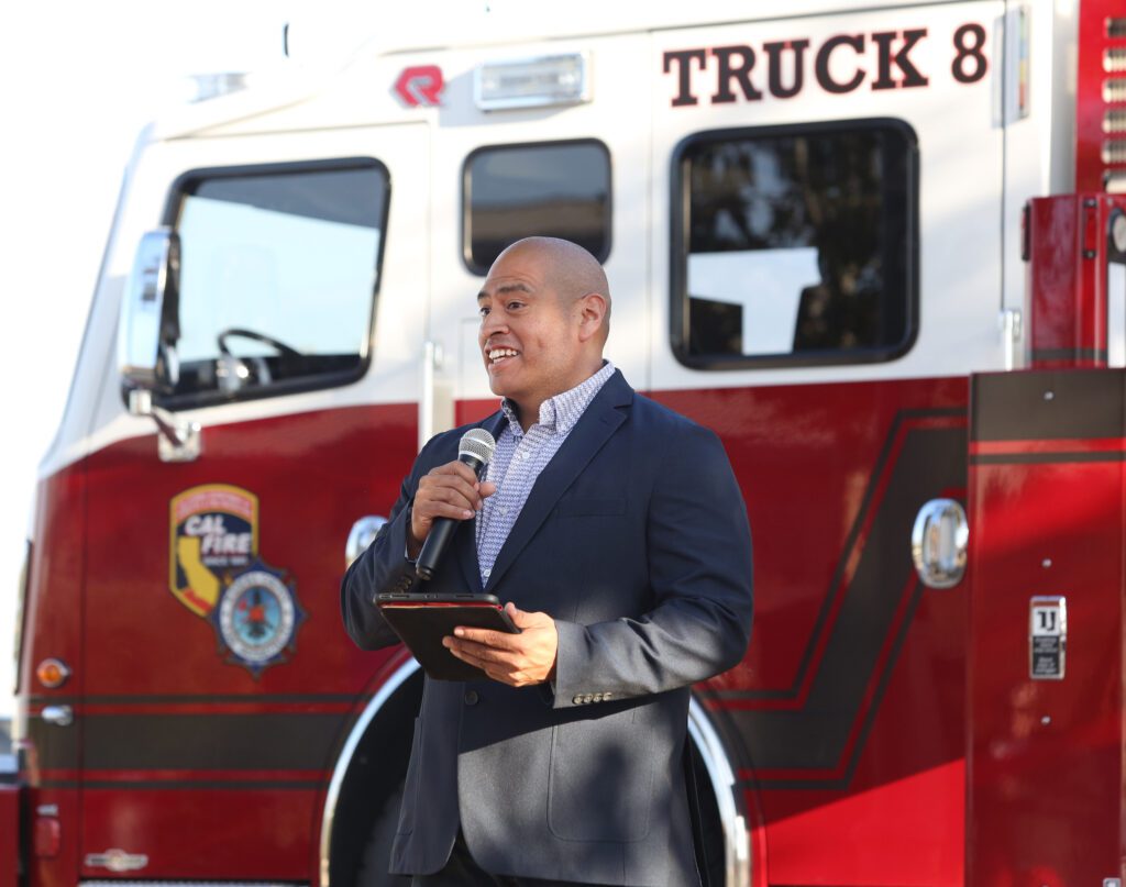 Luis Gaytan, Director of Field Operations in the South Valley Area, for Comcast speaks at Tesoro Viejo's Veterans Day Pancake Breakfast in front of a red and white fire truck.
