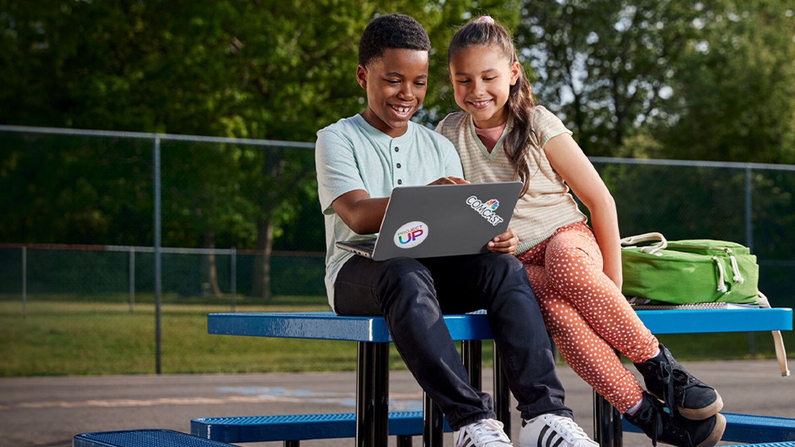 Two young kids sitting on a picnic table looking at a laptop