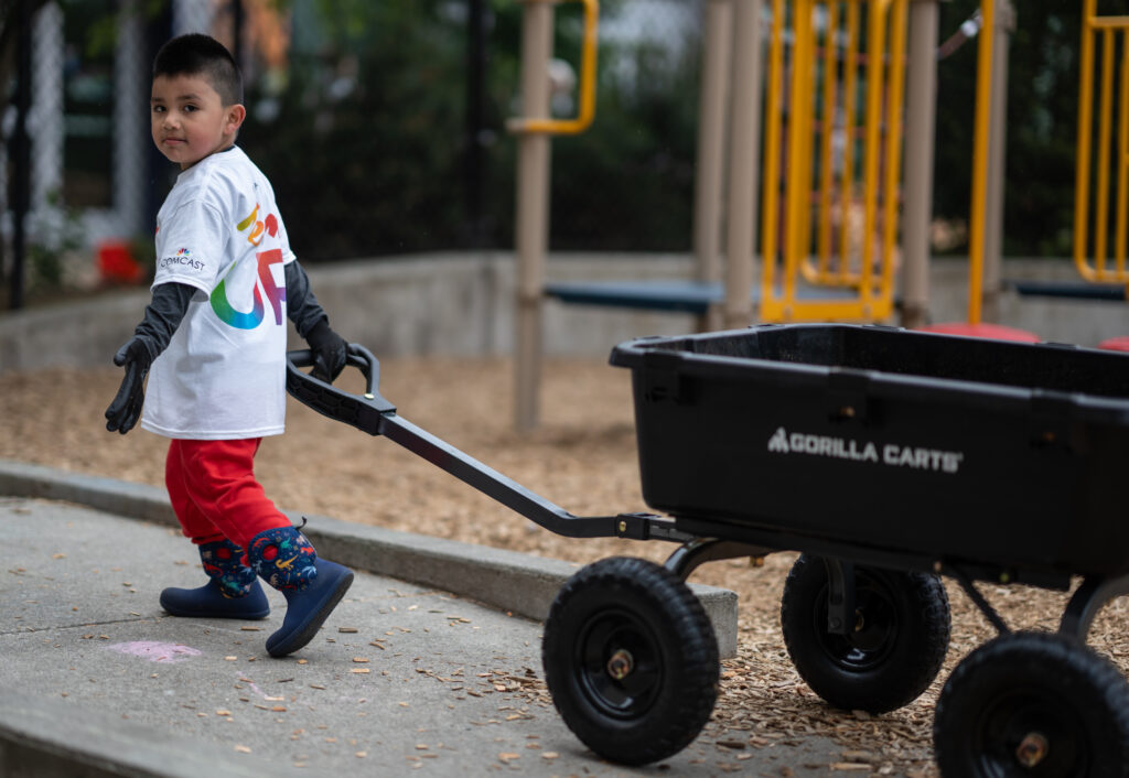 A young boy walks a wheelbarrow at a playground.