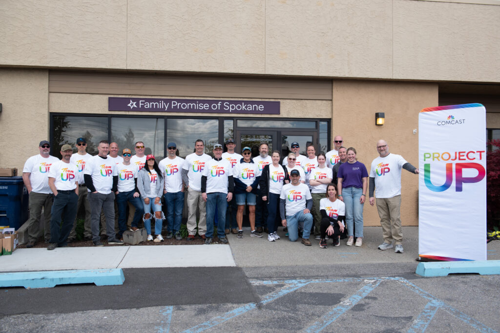 Comcast employee volunteers in front of Family Promise of Spokane wearing Team UP t-shirts.