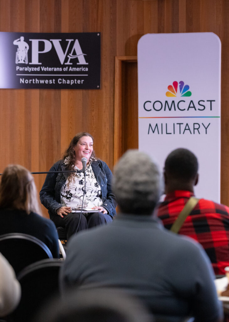 A woman sits next to a Comcast Military sign.