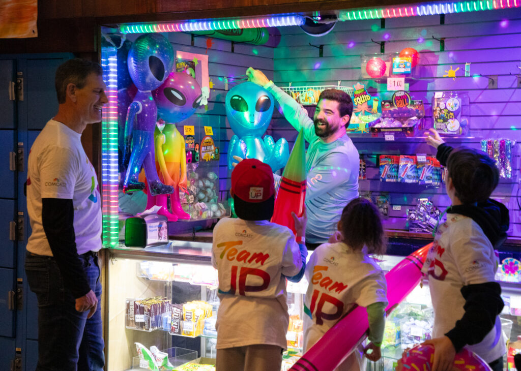 Comcast volunteers and children have fun at a prize area of a gaming center.