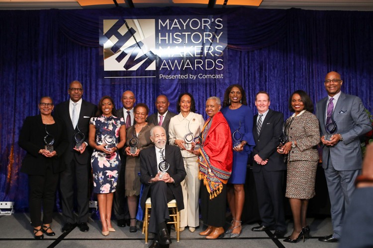 A group of people posing for a photo in front of a large 'Mayor's History Makers Awards Luncheon' logo.