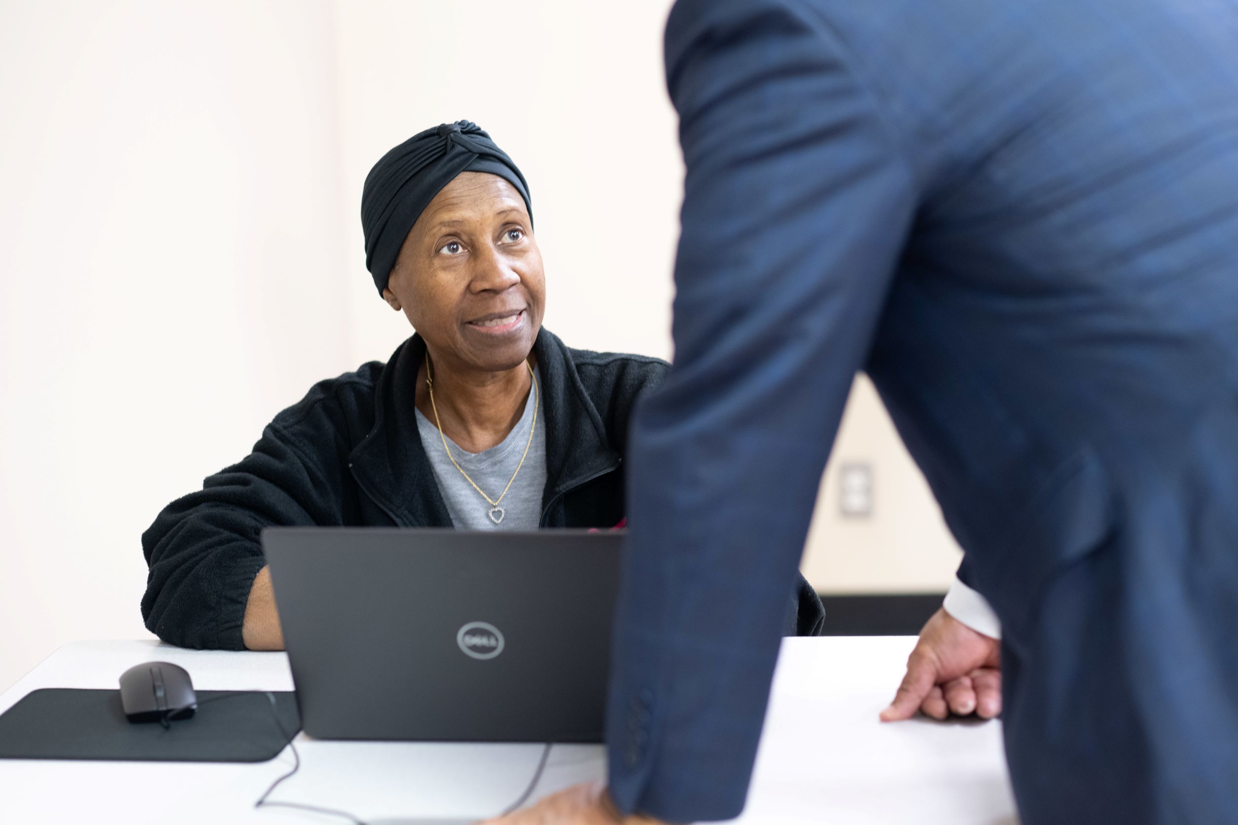 Older African American women sitting in front of laptop, looking up at gentlemen leaning near table.