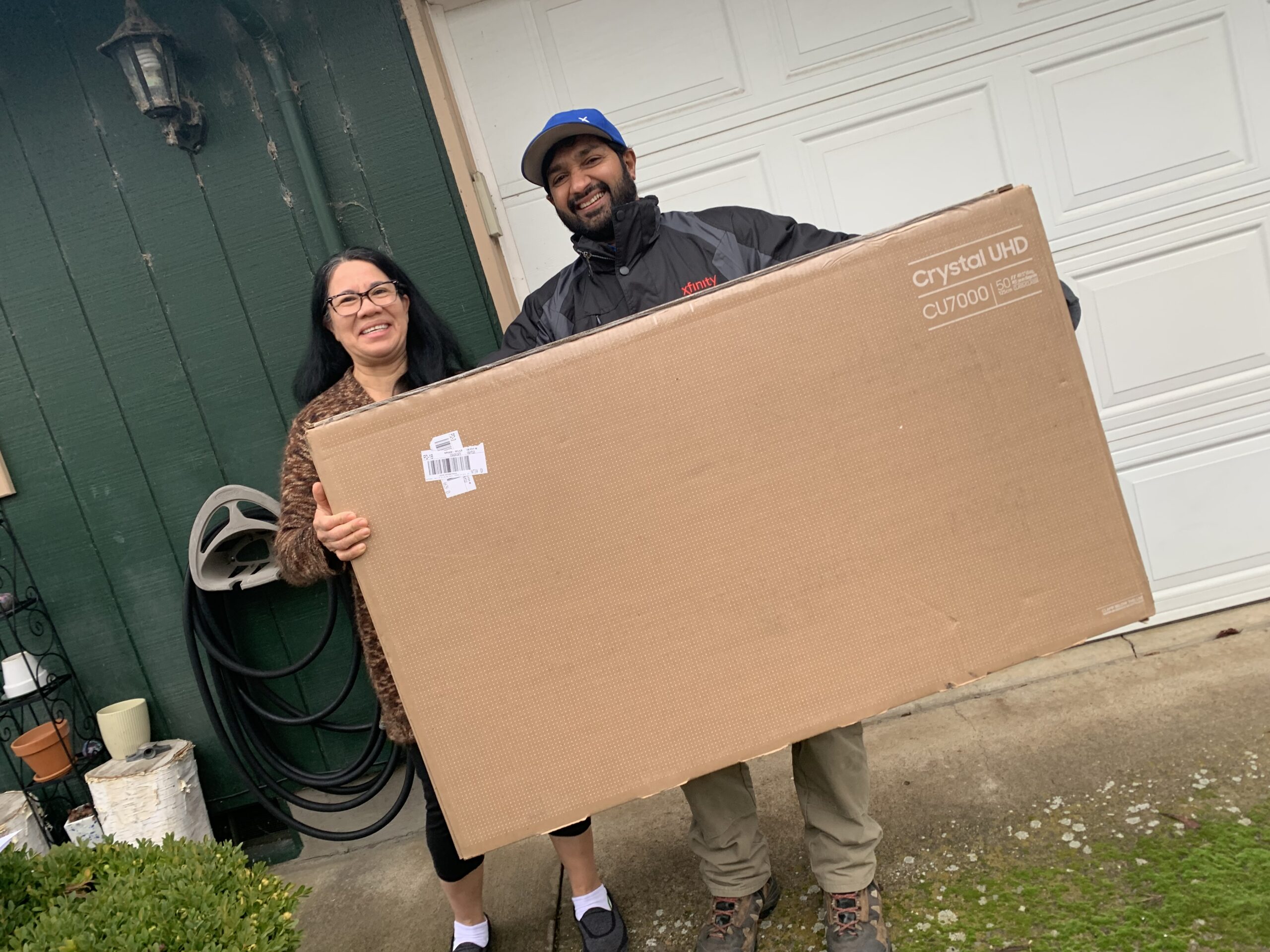 A Comcast customer with a TV outside their home with a Comcast employee.