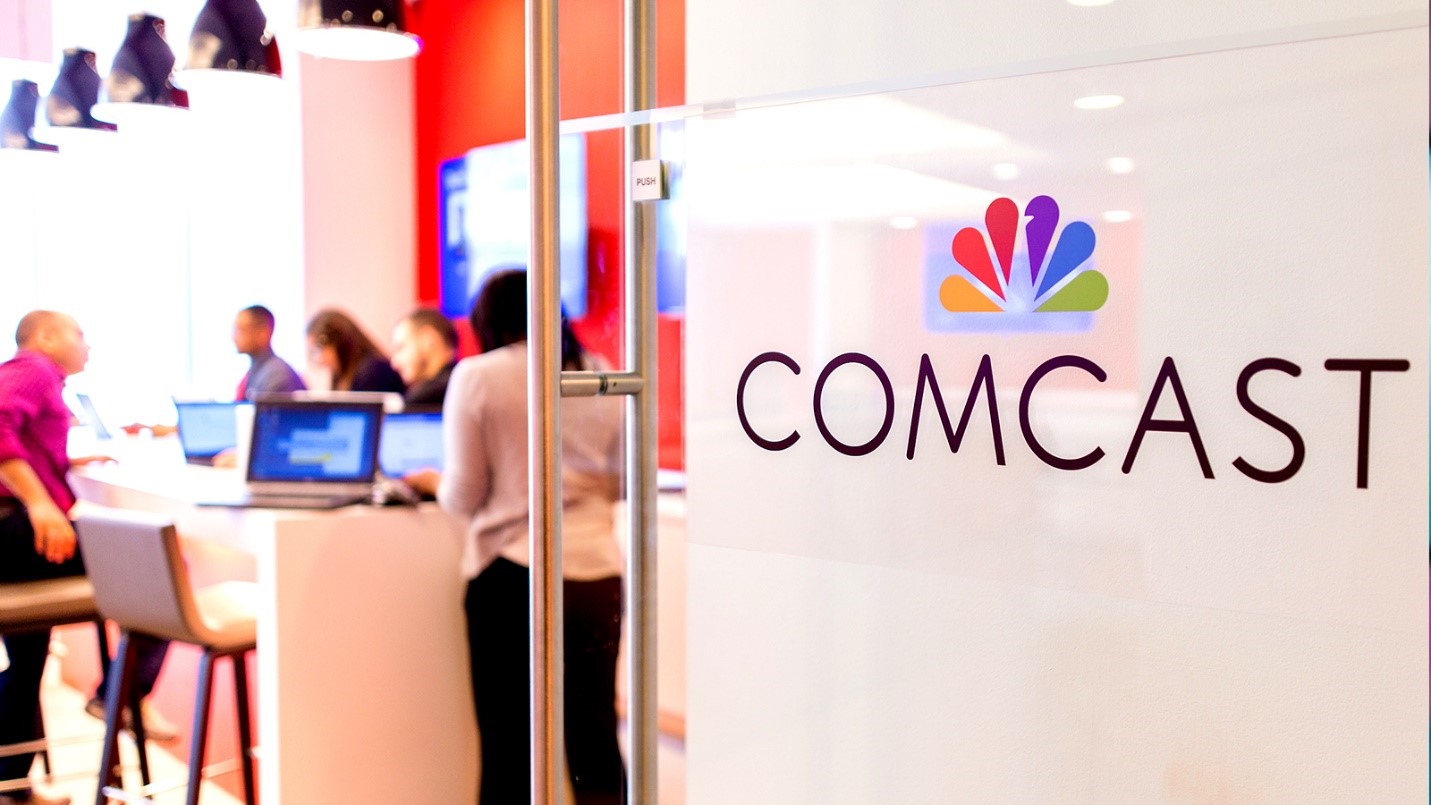 The Comcast logo on a glass door that opens into an employee workspace.