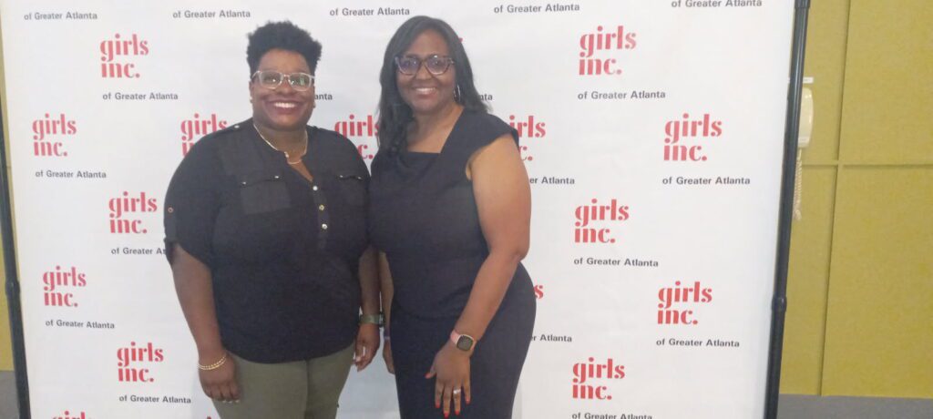 Two women stand in front of a step and repeat to celebrate National Volunteer Month