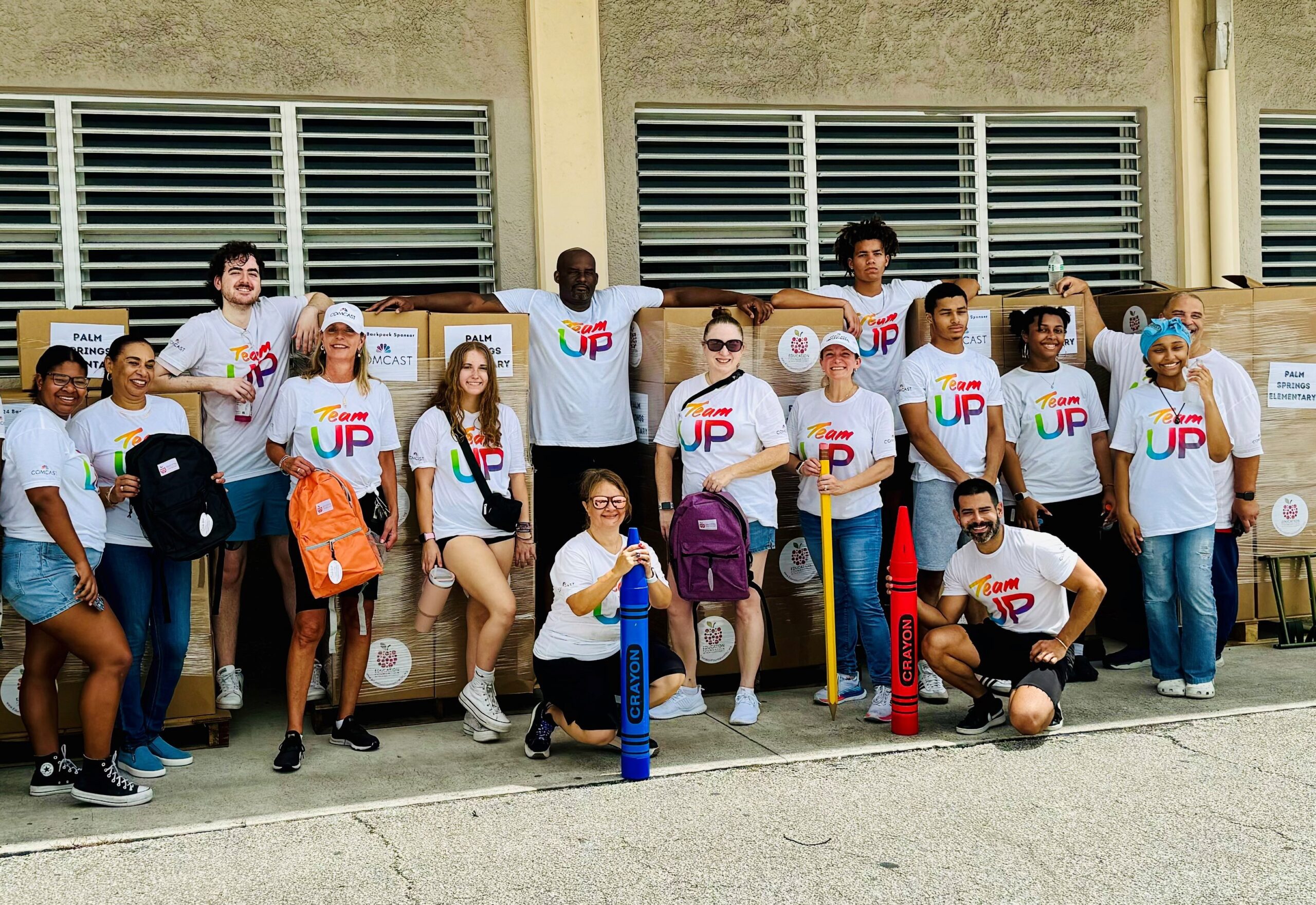 Group of volunteers pose in front of boxes filled with backpacks