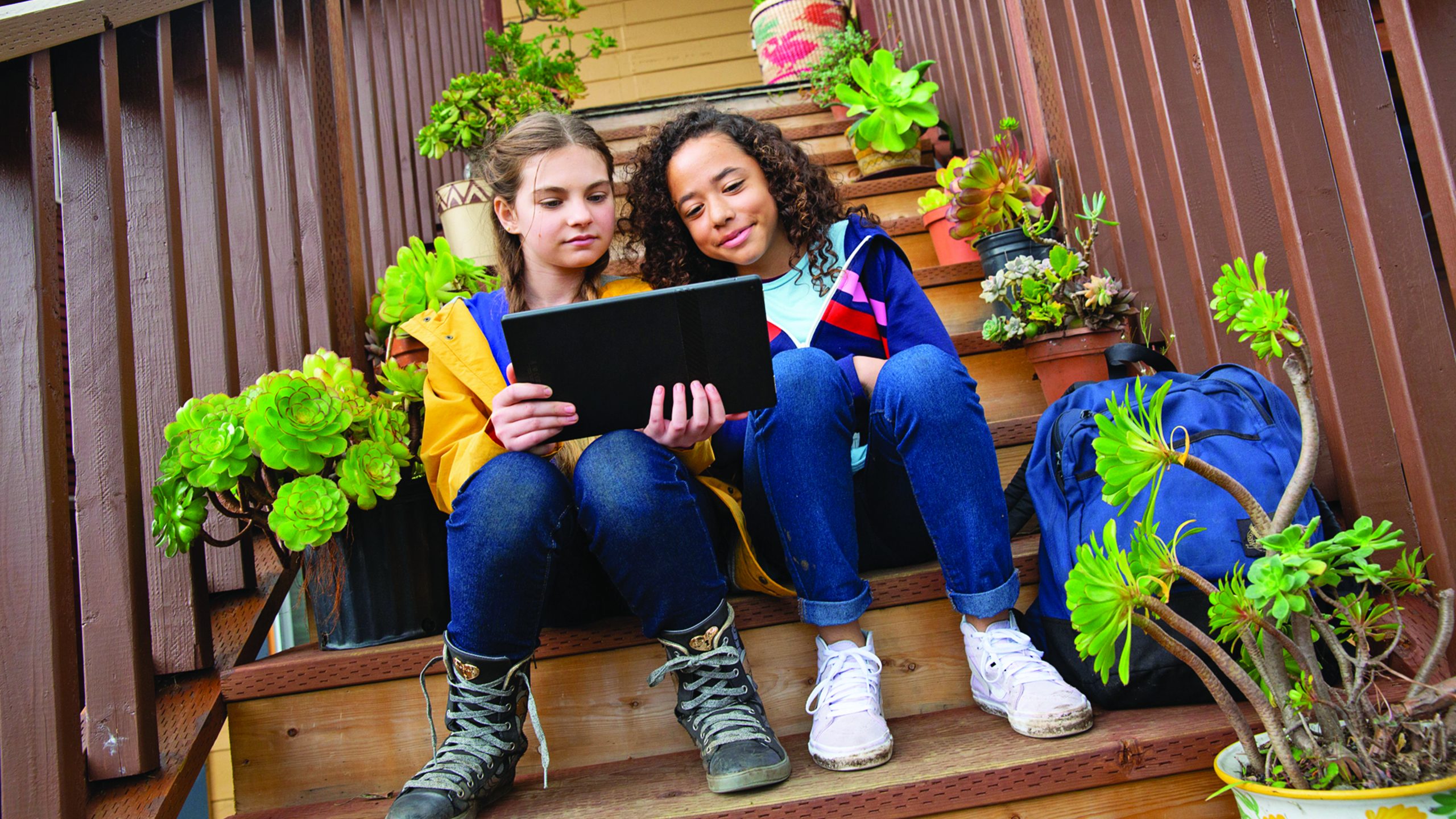 two girls sitting on outdoor steps, looking at a laptop screen