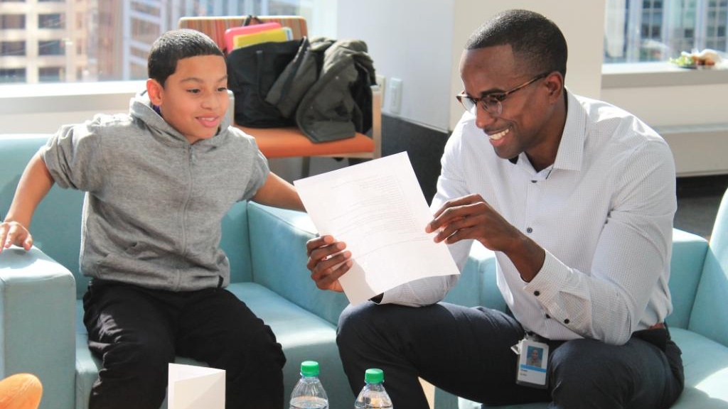 A Big Brother and Little Brother sit next to each other and read a document together.