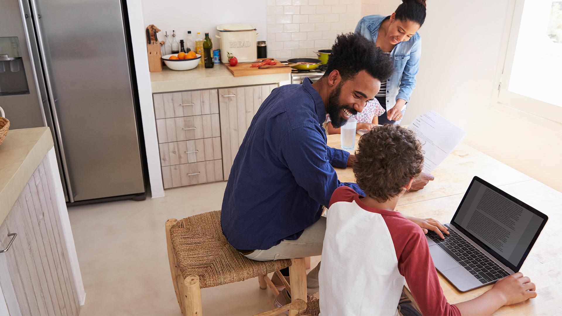 a woman, man and two children sitting at a table looking at a laptop.