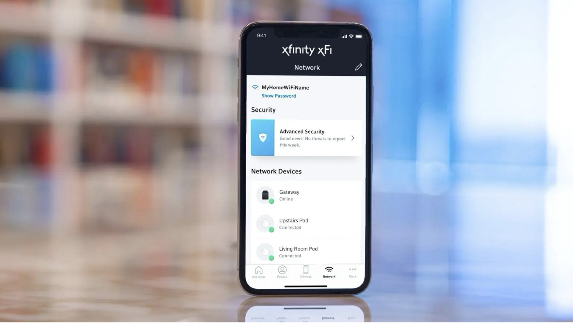 An iPhone displaying the Xfinity xFi app interface. The screen shows network information including a WiFi network name, a security status card showing 'Advanced Security' with 'No threats to report', and a list of connected network devices including a Gateway and two Pods labeled 'Upstairs Pod' and 'Living Room Pod'. The phone is standing on a reflective surface with a blurred background.